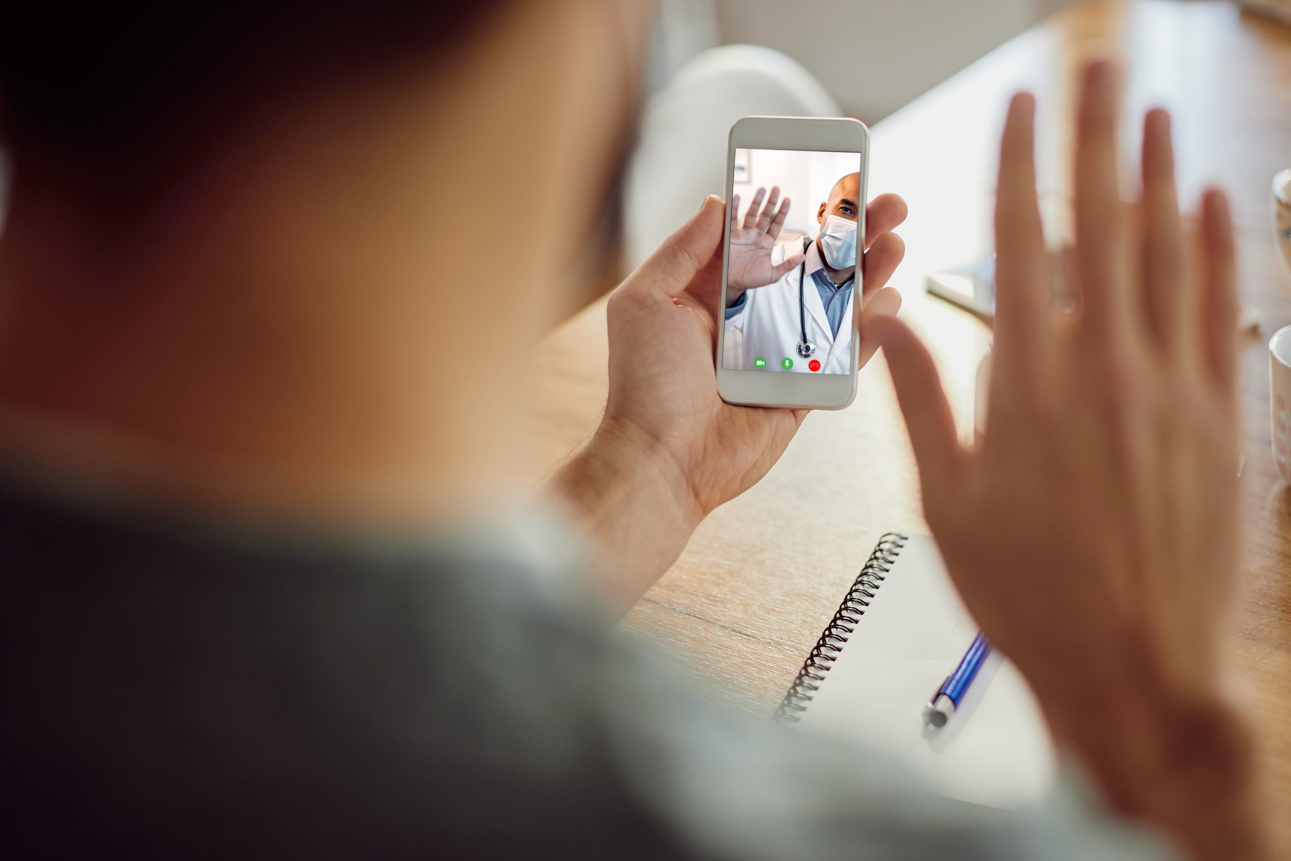 Close-up of a man waving to his doctor during video call over smart phone. Focus is on touchscreen.