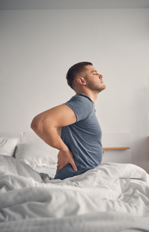 Handsome Caucasian male enjoying day while waking up alone and stretching his back with closed eyes