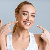 Orthodontic concept. Happy girl showing her beaming white teeth with two forefingers, grey background
