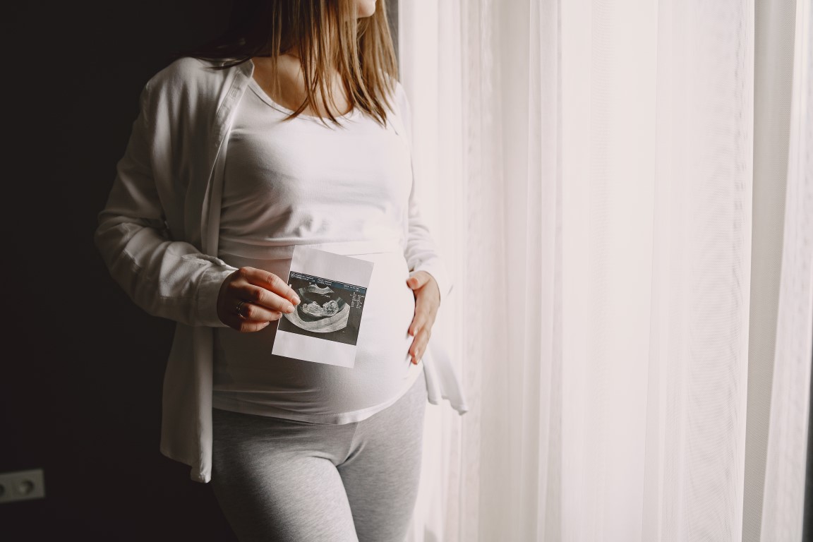 Woman standing by the window. Pregnant looking at photo. Woman expecting a baby.
